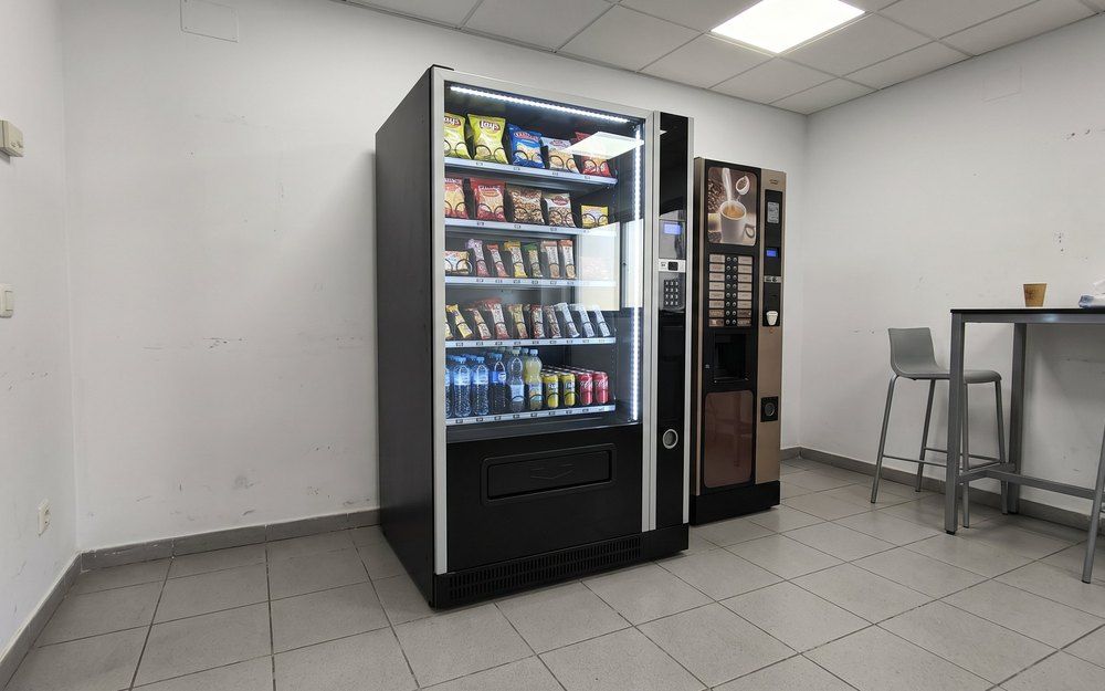 Máquina de vending mixta para empresas con snacks y bebidas frías junto a una máquina de café en la sala de descanso de una oficina